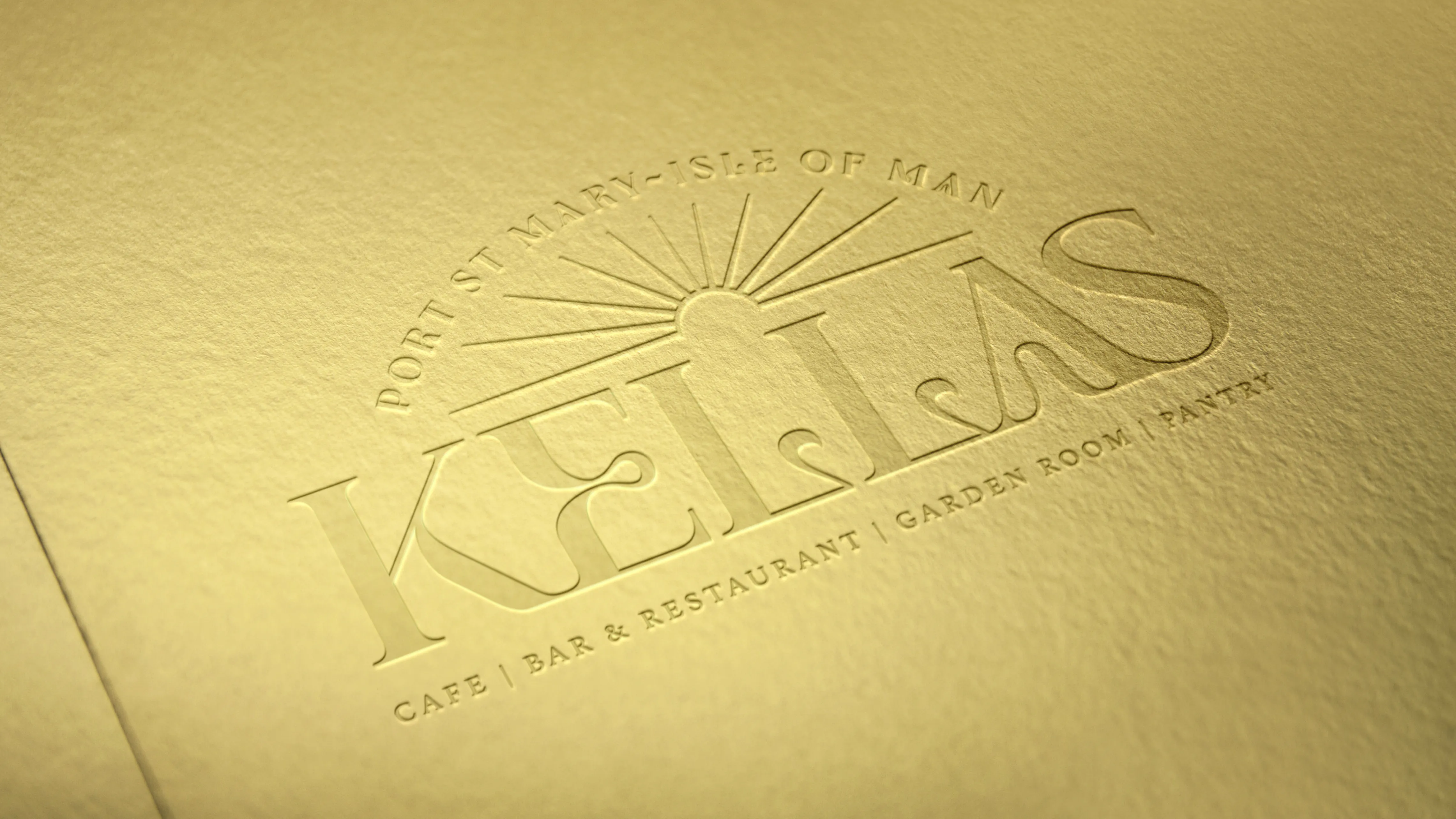A close-up of the Kella's full logo embossed in a tonal deboss/emboss effect on a gold textured card or stationery, featuring the wordmark "Kellas", sunburst motif, "Port St Mary – Isle of Man" arc text, and "Cafe | Bar & Restaurant | Garden Room | Pantry" tagline.
